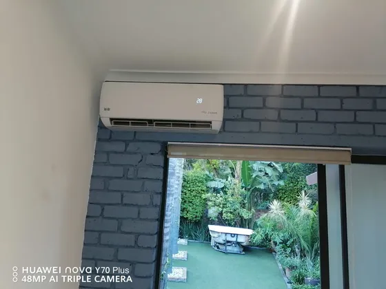 A white indoor unit above a doorway against a blue brick-effect feature wall.