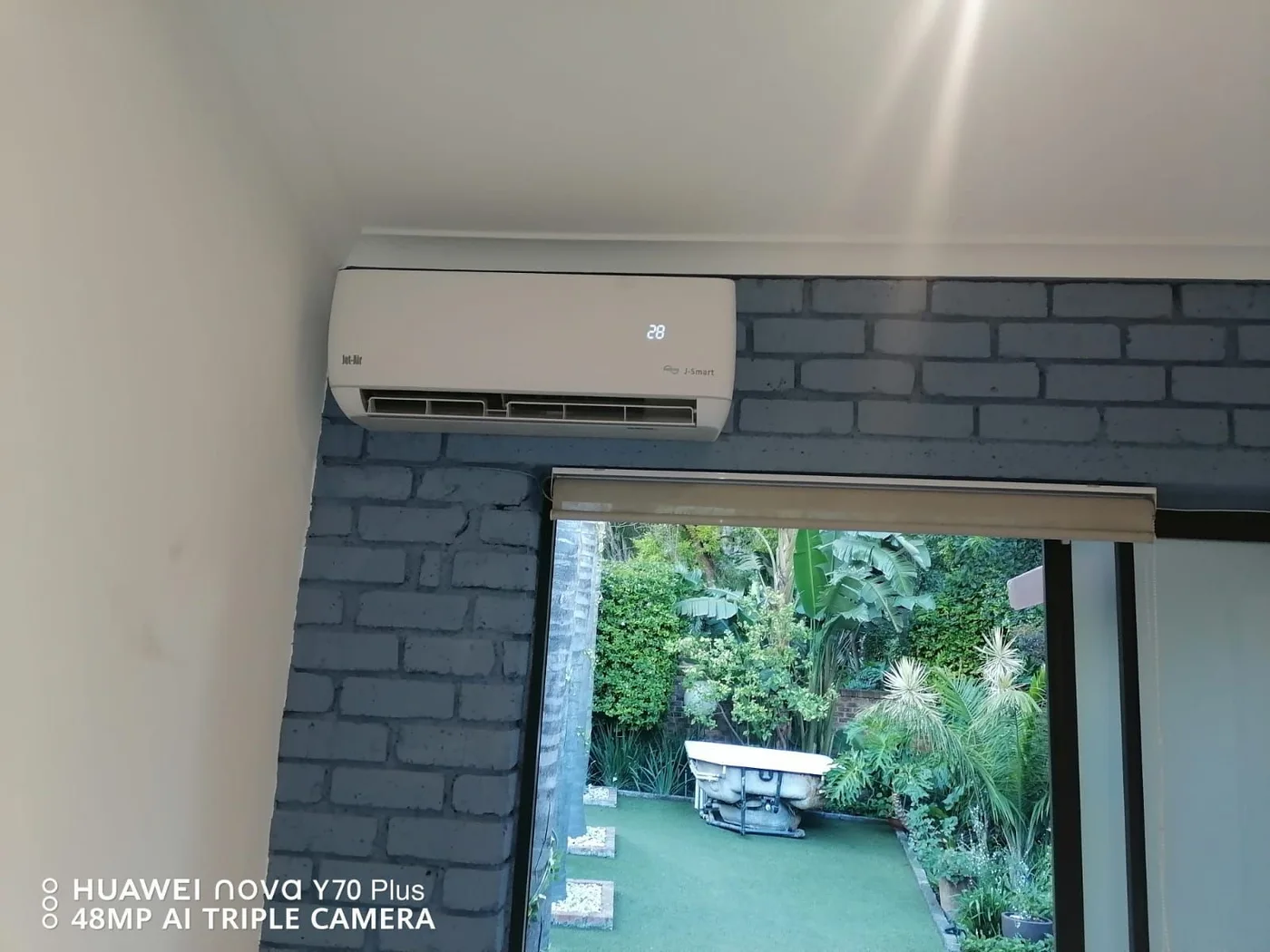 A white indoor unit above a doorway against a blue brick-effect feature wall.