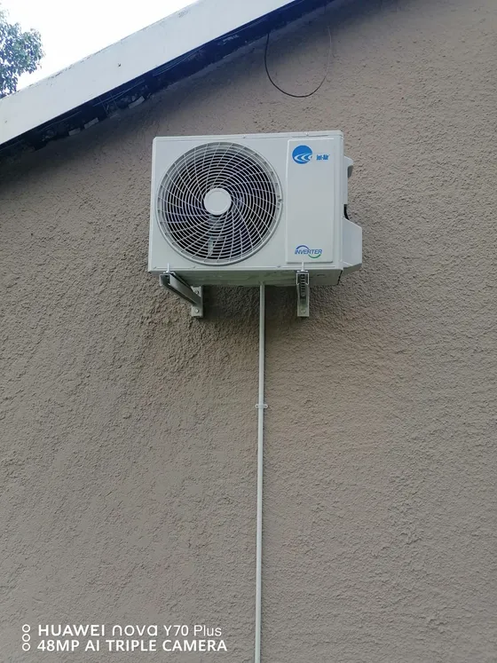 An outdoor air-conditioning unit mounted on brackets with a vertical service route.