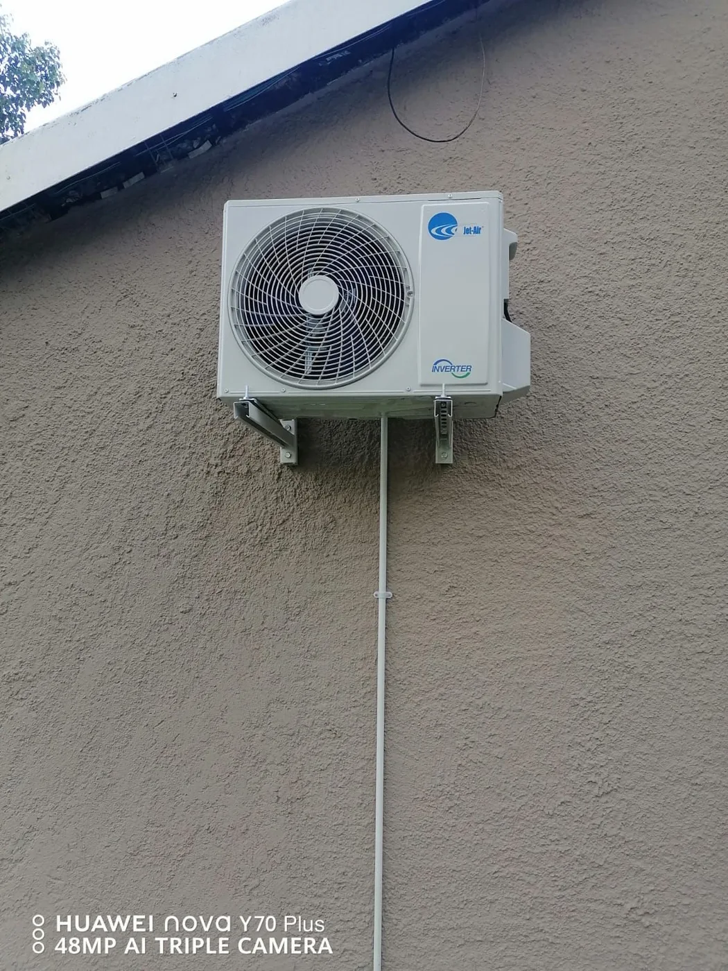 An outdoor air-conditioning unit mounted on brackets with a vertical service route.