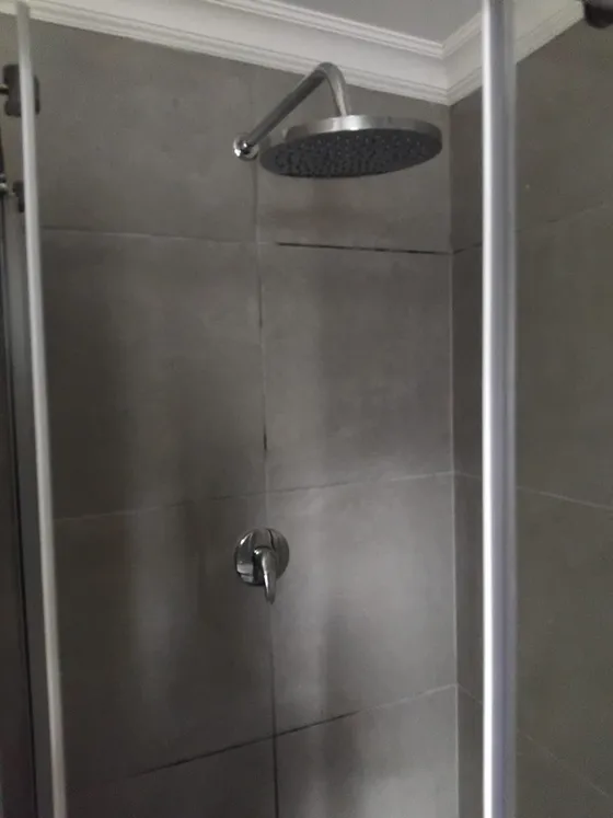 A wall-mounted rain shower against large-format grey tiles.