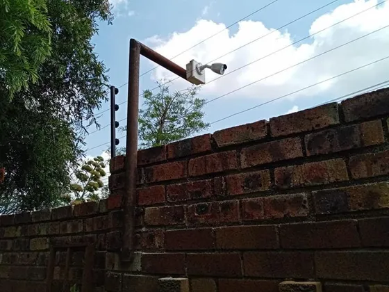 A camera on a raised steel bracket above a brick boundary wall.