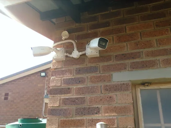 Two cameras mounted on a brick wall beneath the roof overhang.