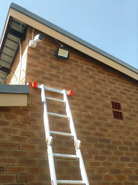 A camera beneath a brick gable with an access ladder in place during installation.