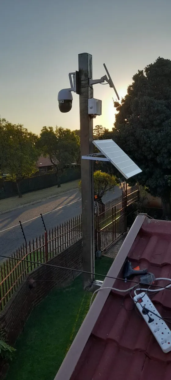 A pole-mounted camera installation with a small solar panel beside a boundary road.