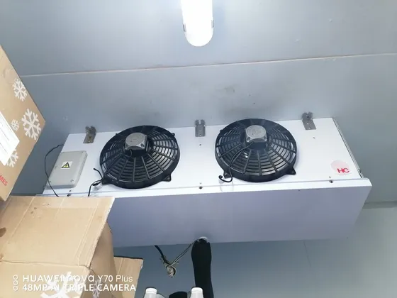 A twin-fan cooling unit fitted high inside an insulated storage room.