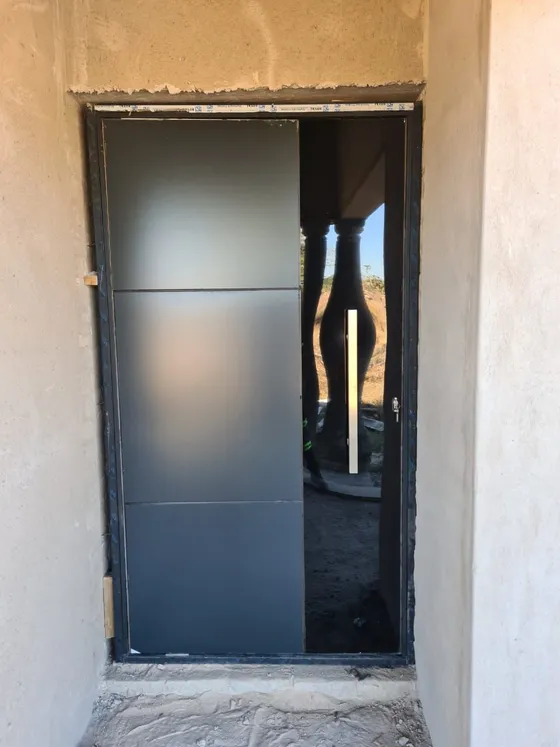 A dark entrance door and glazed side panel within an opening with unfinished plasterwork.