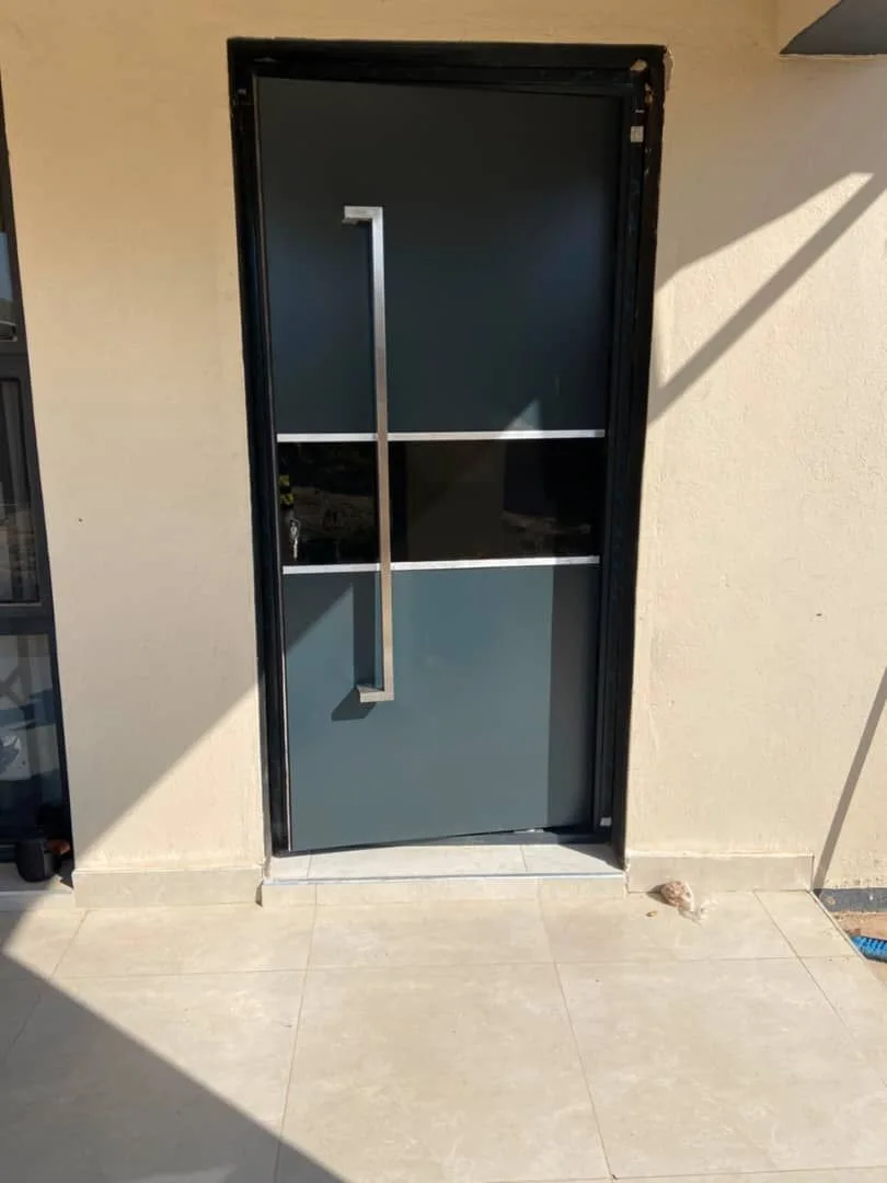 A dark entrance door with horizontal glazing and a long silver handle in a beige wall.