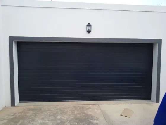 A wide black sectional garage door framed by a white exterior wall.