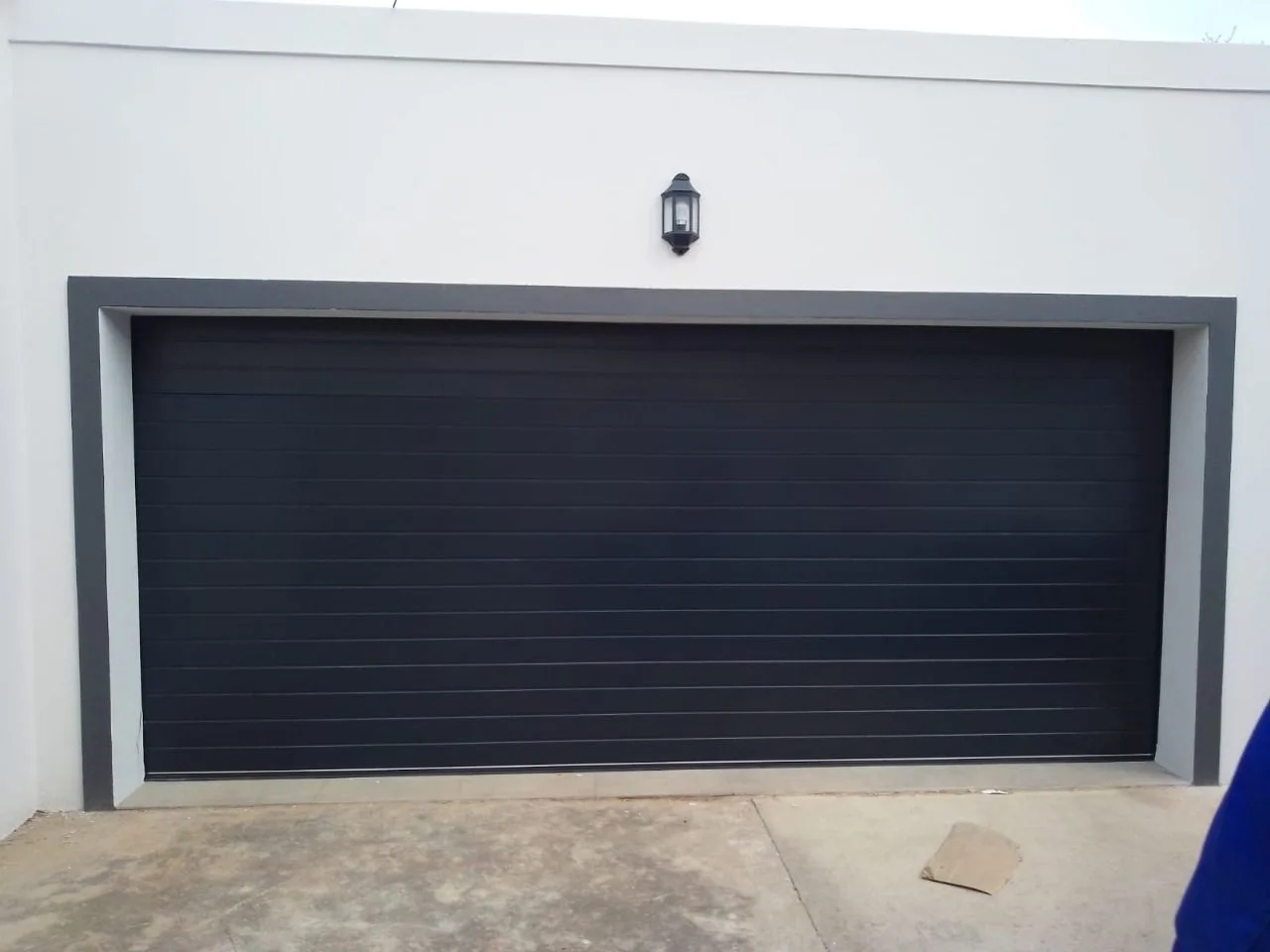 A wide black sectional garage door framed by a white exterior wall.