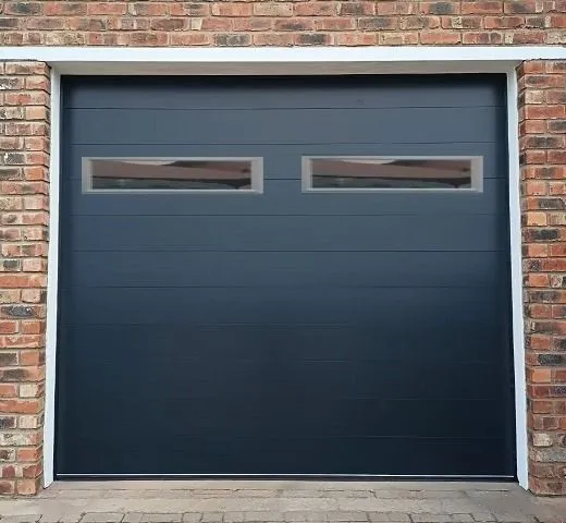A dark single garage door with two horizontal windows in a face-brick wall.