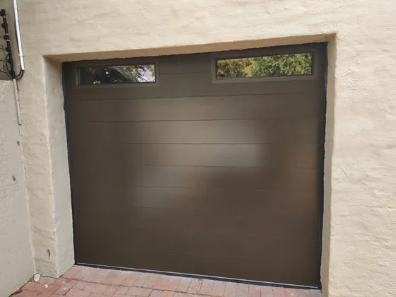 A brown single garage door with two upper windows set into a plastered wall.
