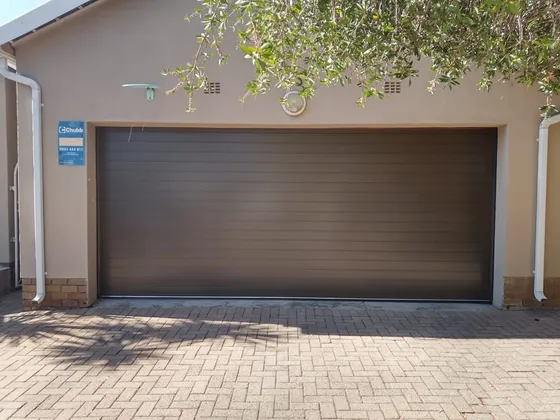 A brown sectional garage door beneath a tiled roof, opening onto a paved driveway.