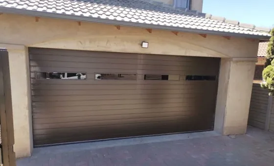 A wide brown garage door with a row of narrow windows beneath a tiled roof.