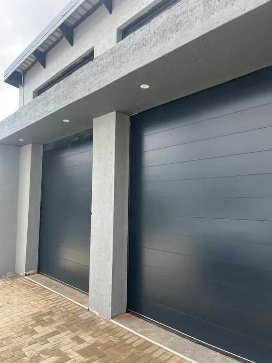 An angled view of two charcoal garage doors beneath a concrete-grey facade.