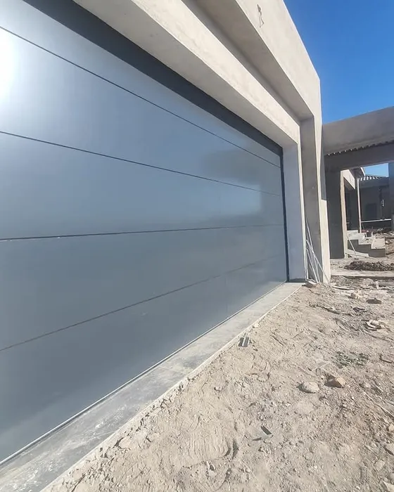 A close angled view of a grey garage door with the ground outside still unfinished.