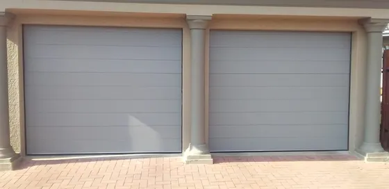 Two light-grey garage doors side by side above a paved driveway.