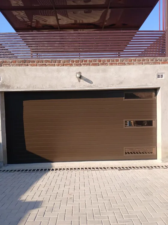 A brown garage door below a covered balcony, with the wider building facade in view.