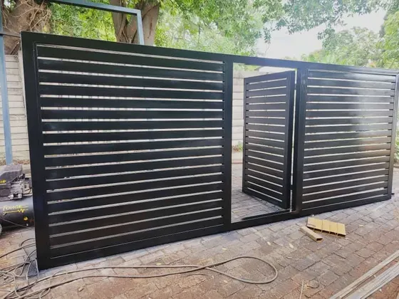 A dark horizontal-slatted gate with an integrated pedestrian door partly open above paving.