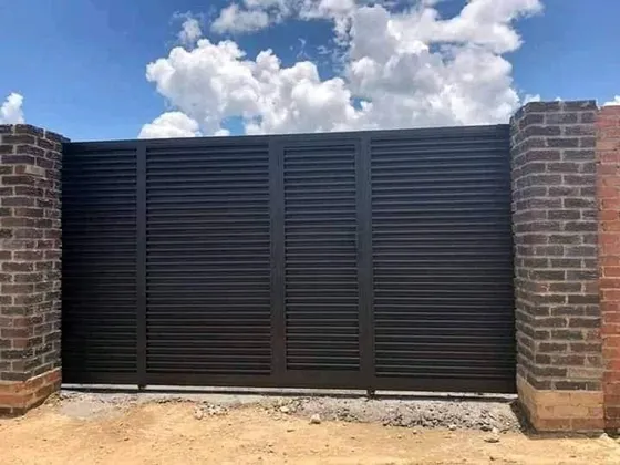 A dark horizontal-slatted driveway gate fitted between brick pillars.