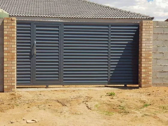 A dark driveway gate combining horizontal slats and solid vertical panels between brick pillars.