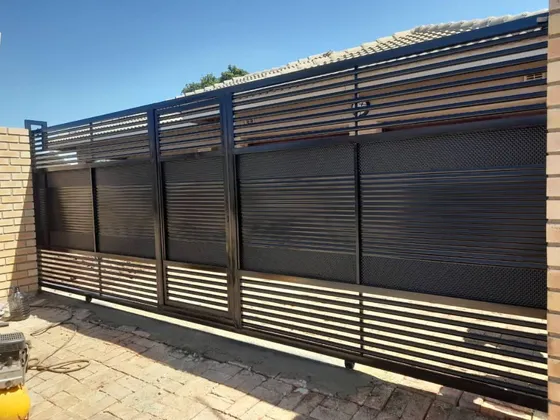 A dark driveway gate with solid central panels and horizontal openings along the top and bottom.