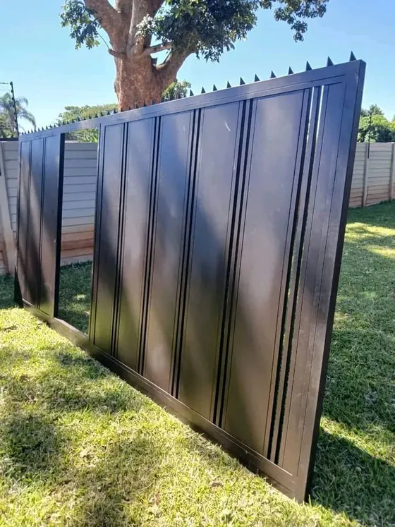 An angled view of a dark gate with solid vertical panels beside a lawn.