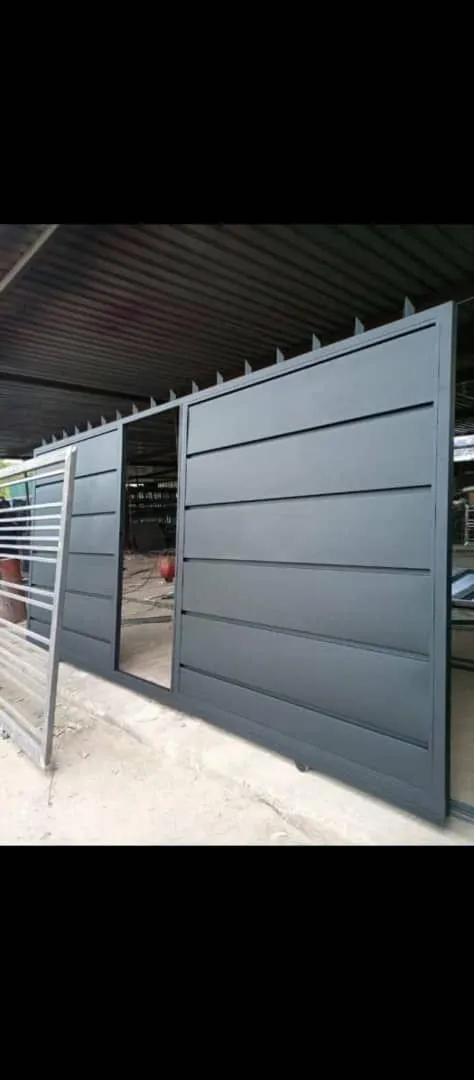A grey gate with horizontal solid panels and a pedestrian opening beneath a workshop roof.
