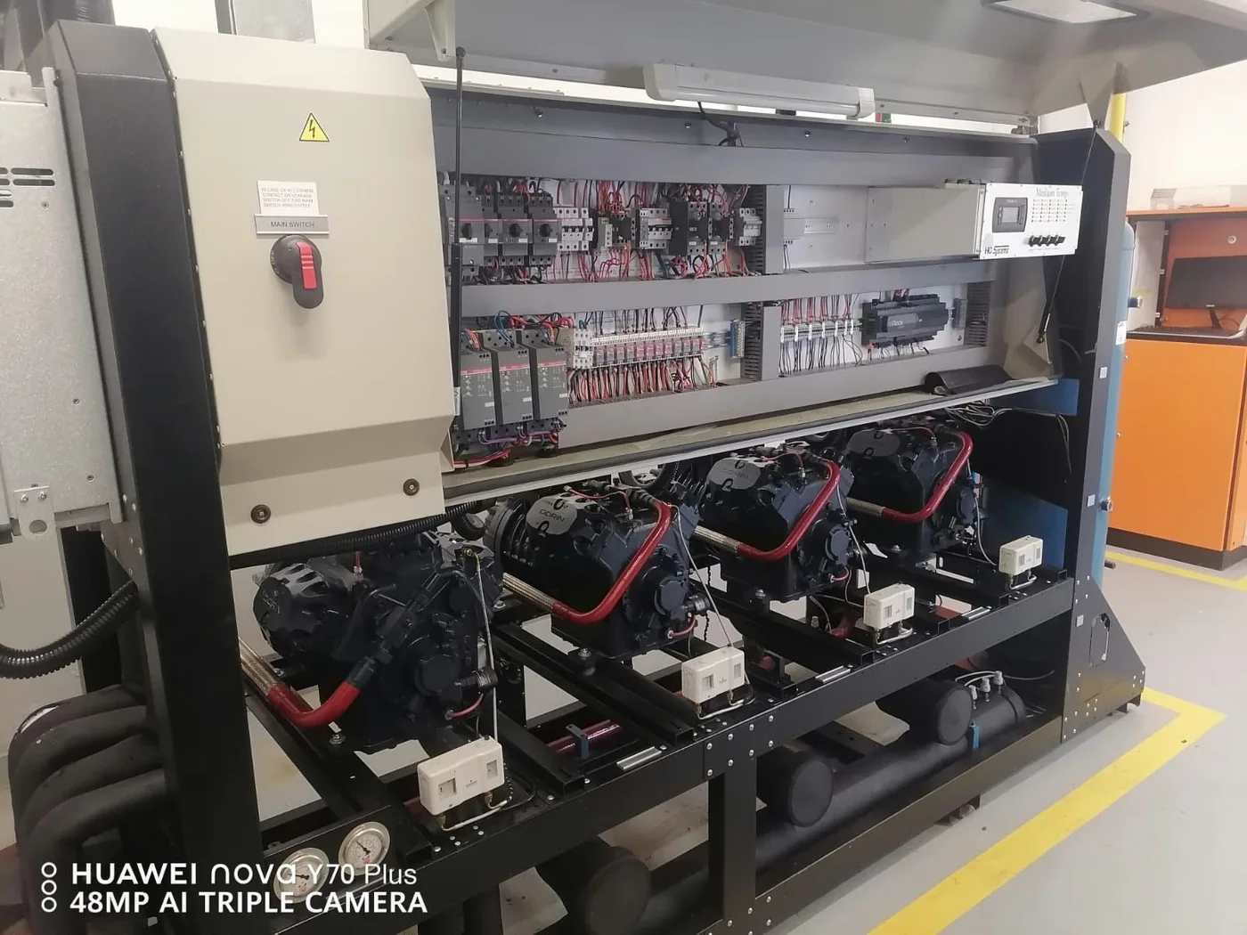 A wider equipment view with compressors, pipework and the open control cabinet above.