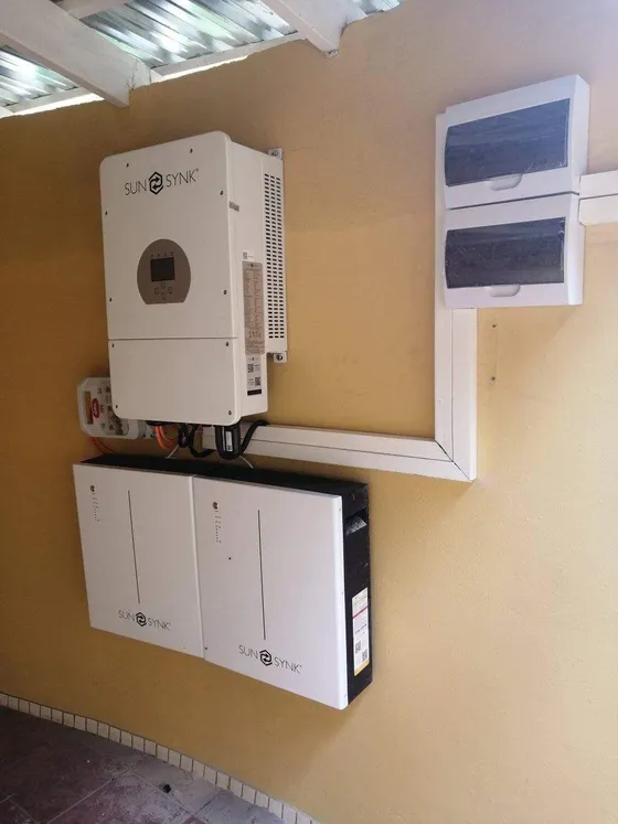 White inverter above two battery units beside distribution boards and cable trunking.