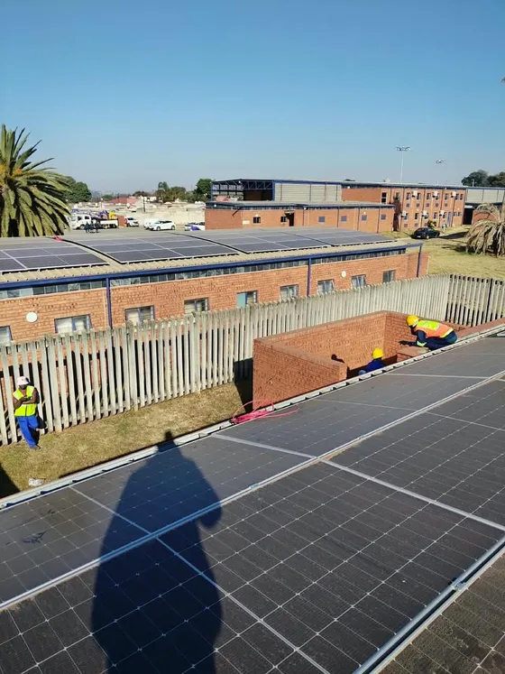 Rooftop solar panels with installers wearing high-visibility clothing nearby.