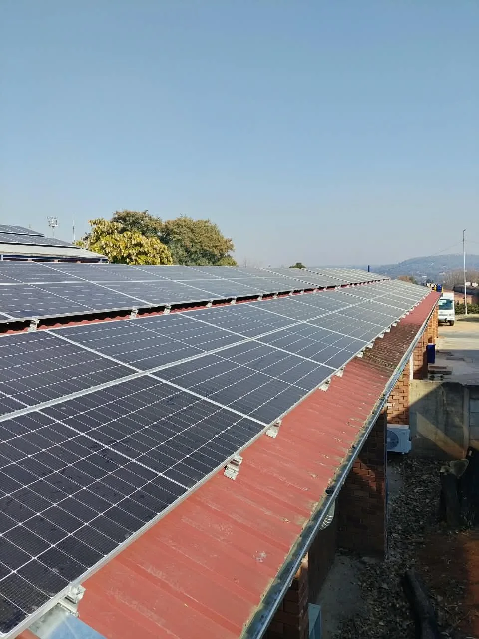 Solar panel array on a red metal roof under a clear blue sky.