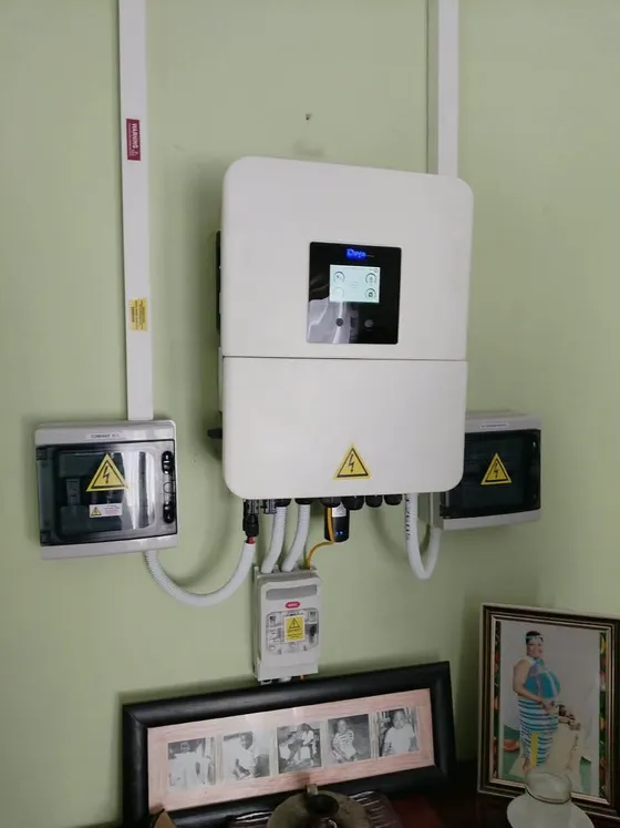 White inverter on a green wall with adjacent electrical enclosures and cable conduits.