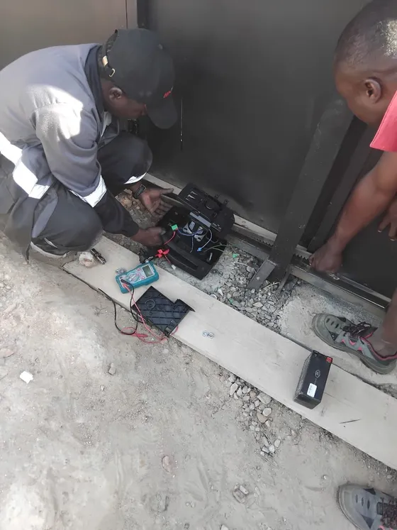 Gate-motor components and tools beside a sliding gate during work.