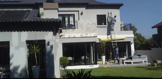Exterior wall preparation with workers and ladders beside a house.