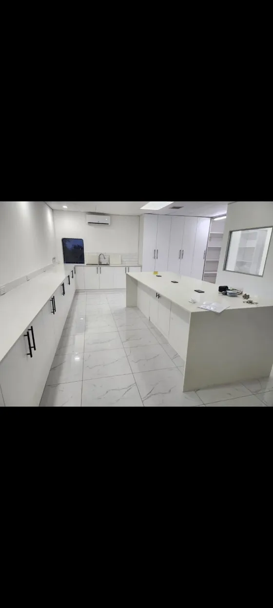 White kitchen cupboards, worktops and an island in a tiled room.