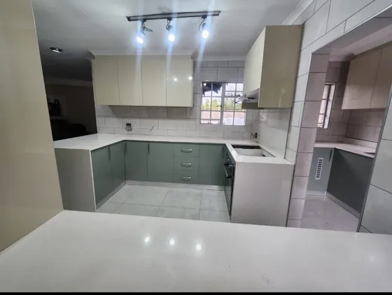 A kitchen with grey cupboards, light worktops and tiled walls.