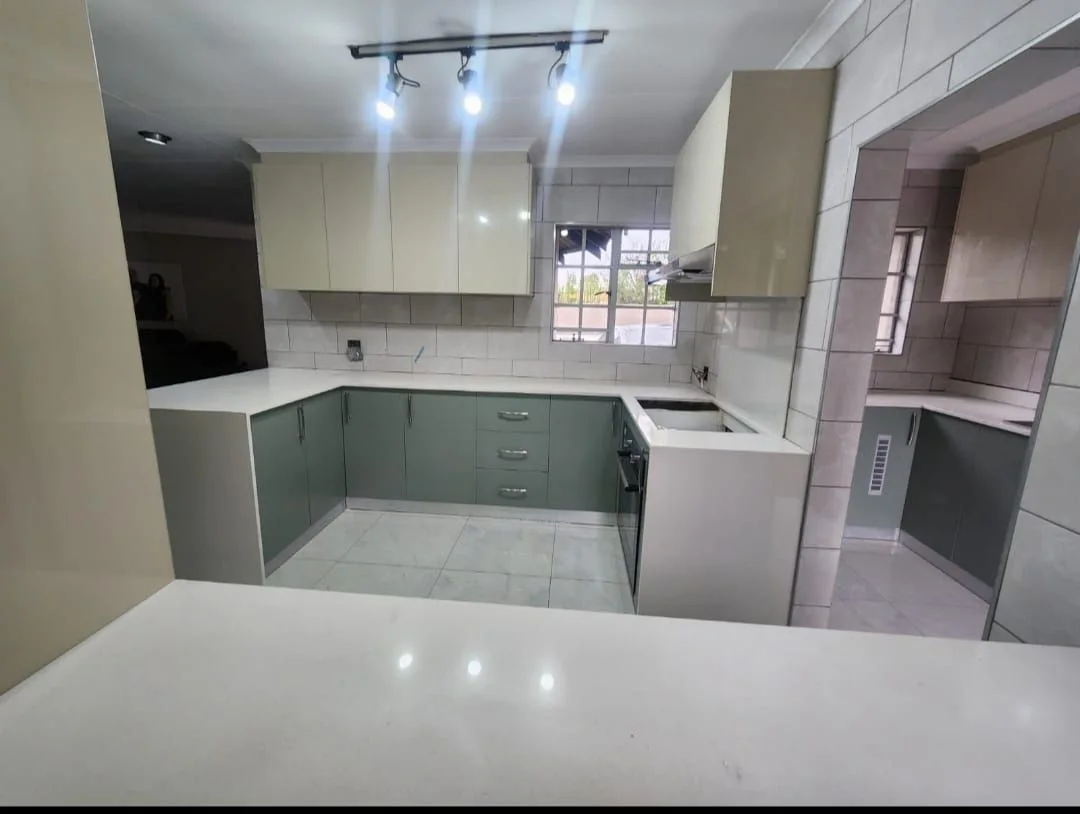 Kitchen with muted green cabinetry, white worktops and tiled walls
