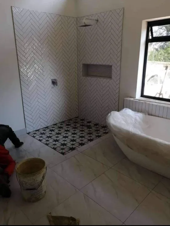 A tiled bathroom with a freestanding bath and shower area during finishing.