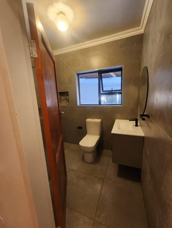 A narrow bathroom with a toilet, vanity and patterned wall finishes.