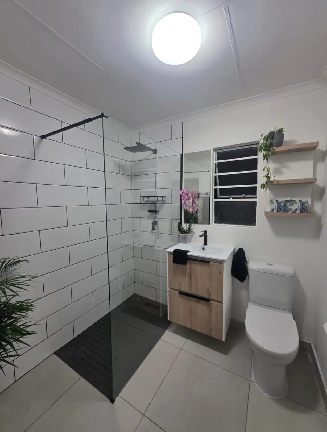 Bathroom with a glass shower screen, black fittings and a timber vanity
