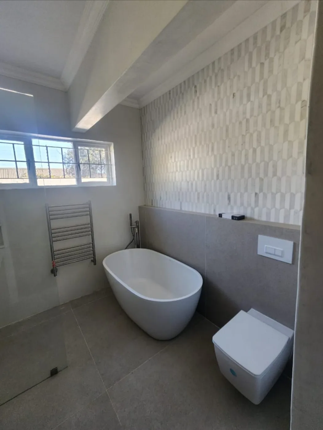 A freestanding bath and wall-mounted toilet against tiled walls.