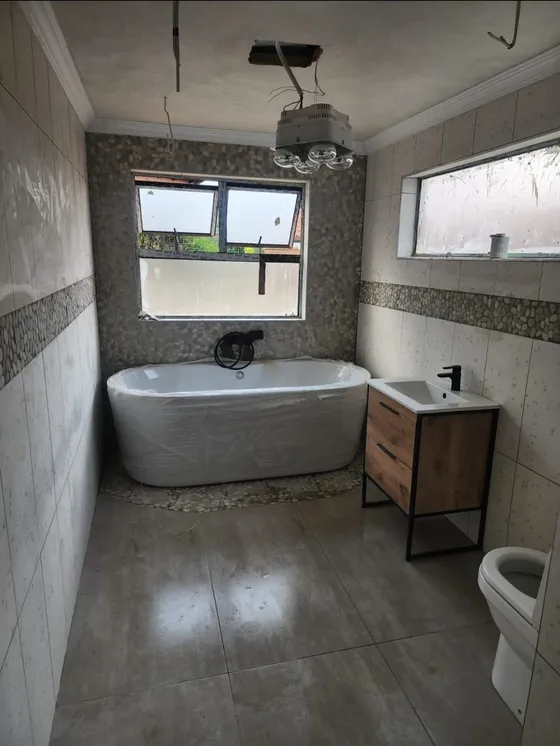 A freestanding bath and vanity beneath large bathroom windows.