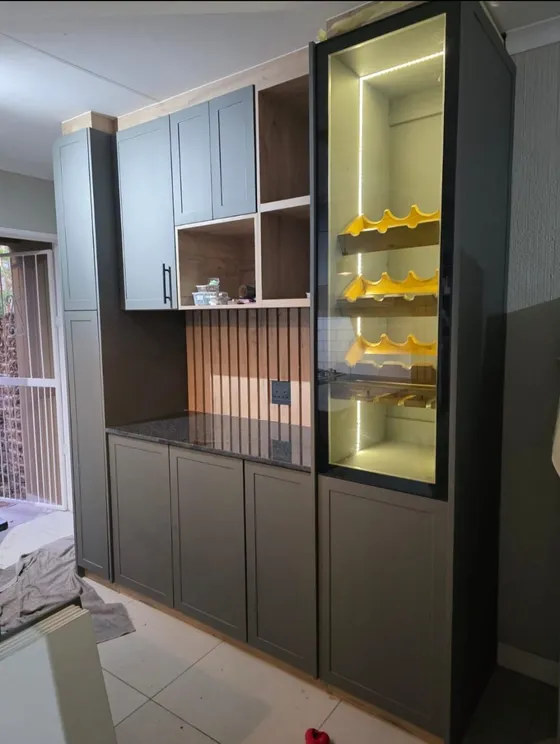 A tall illuminated display cabinet beside fitted kitchen cupboards.