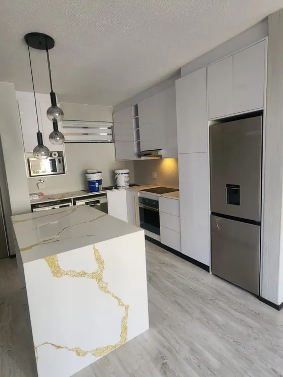 A light kitchen island with pendant lights and fitted cabinetry behind it.